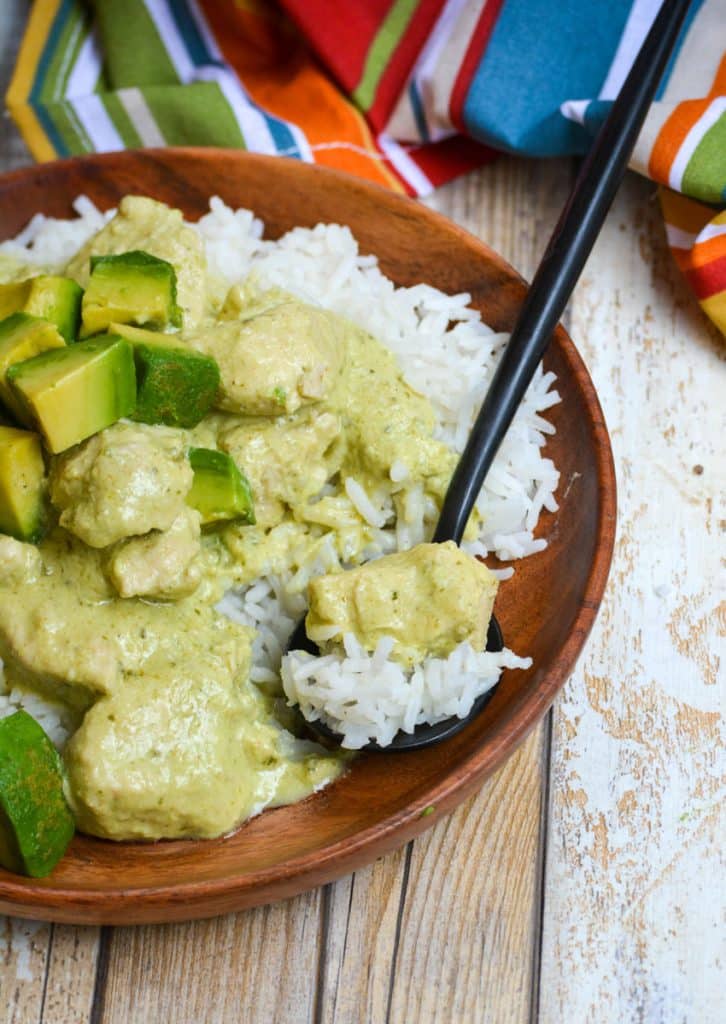 a piece of creamy avocado chicken and steamed white rice on a black fork resting on a wooden plate