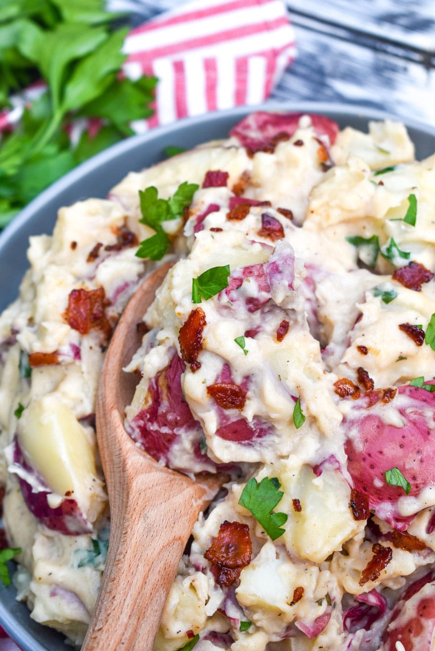 a wooden spoon scooping creamy bacon ranch red potatoes out of a gray bowl