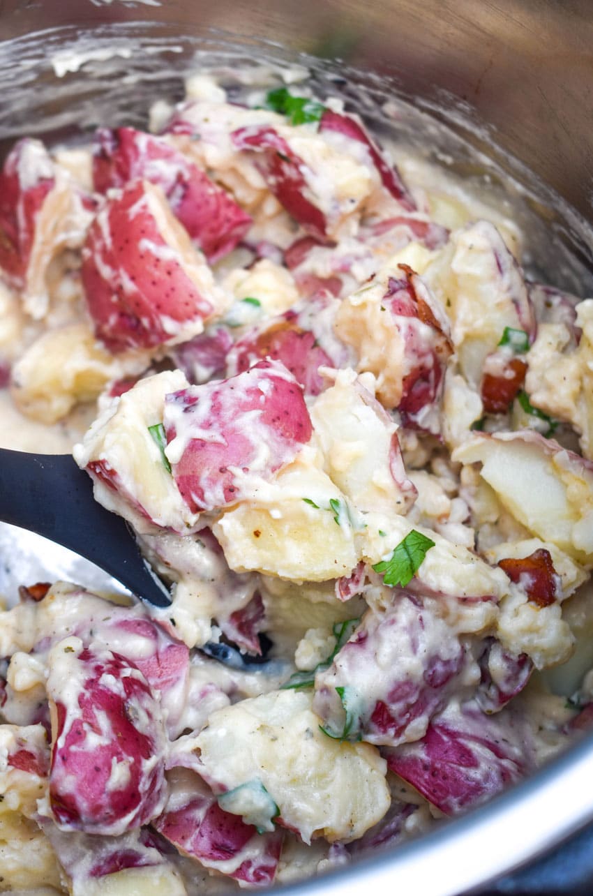 a black spoon scooping creamy bacon ranch potatoes out of an instant pot