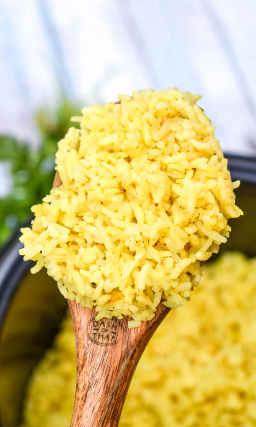 a wooden spoon holding up a scoop of instant pot yellow rice