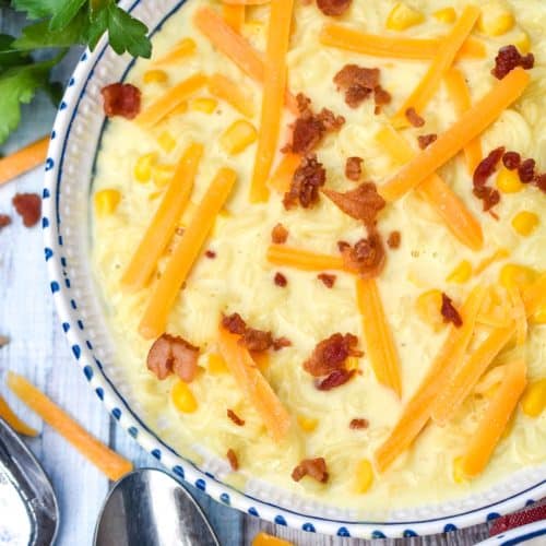 ramen noodle chowder topped with shredded cheese and bits of bacon in a white and blue flecked bowl