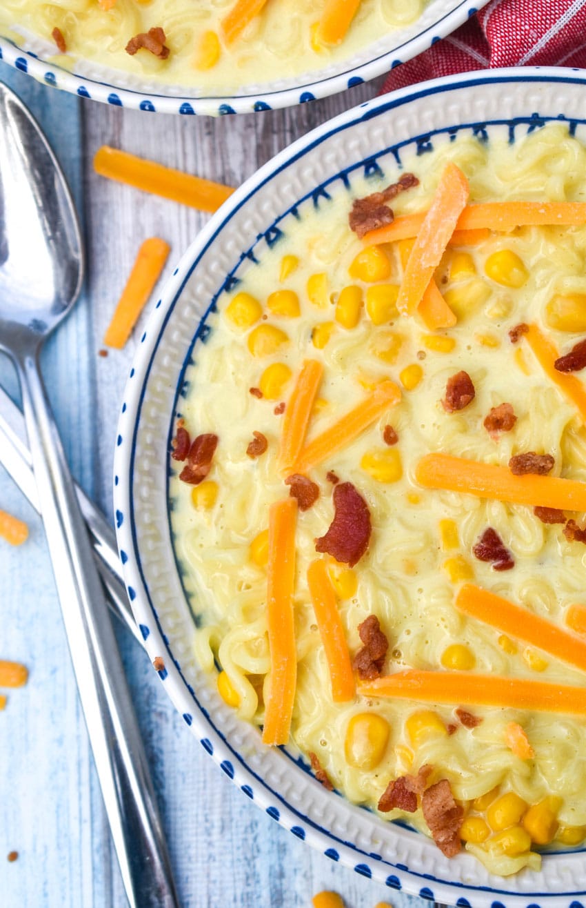 ramen noodle chowder topped with shredded cheese and bits of bacon in a white and blue flecked bowl