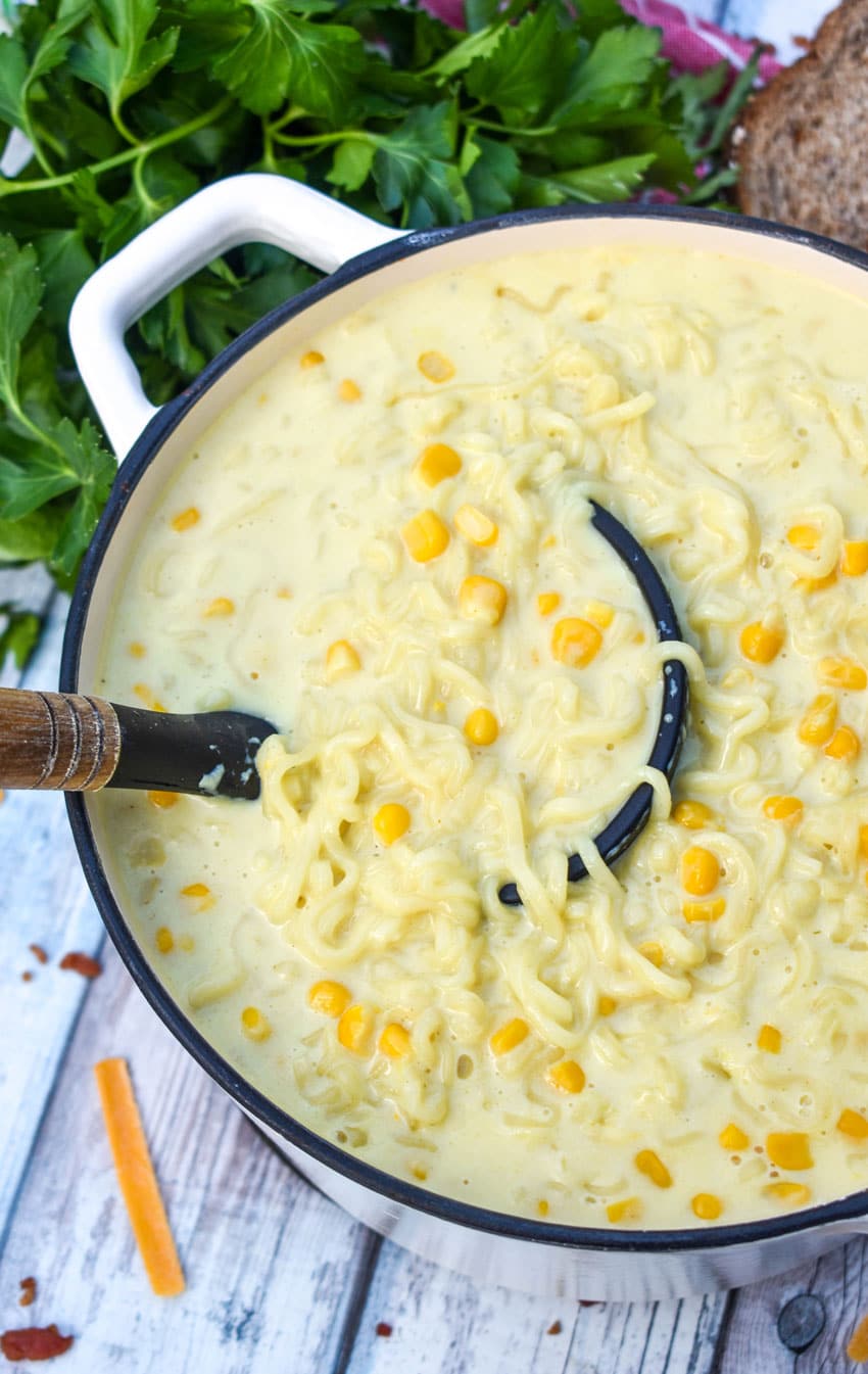 a black silicone spatula scooping ramen noodle chowder out of a white cast iron pot