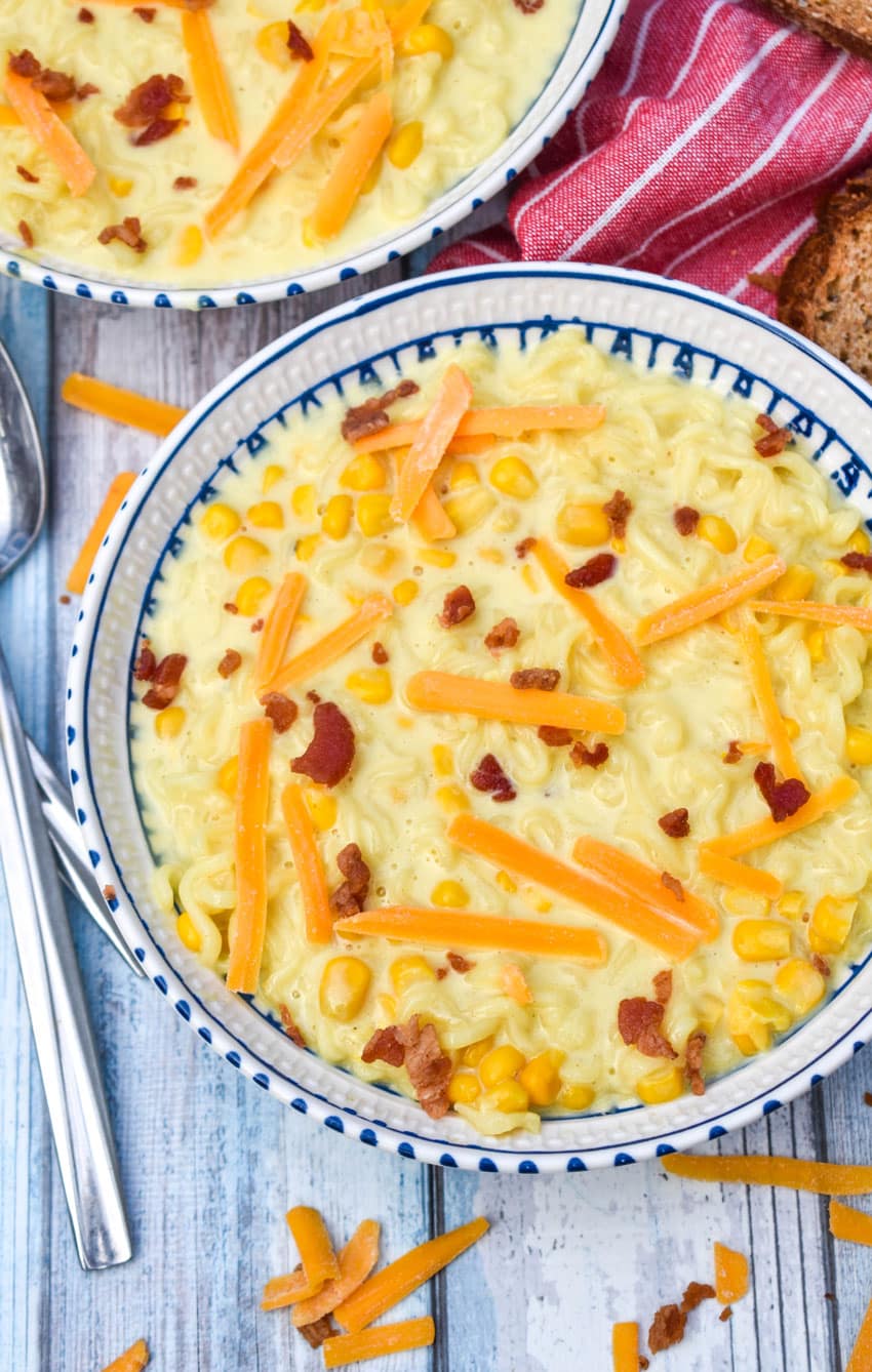 ramen noodle chowder topped with shredded cheese and bits of bacon in a white and blue flecked bowl