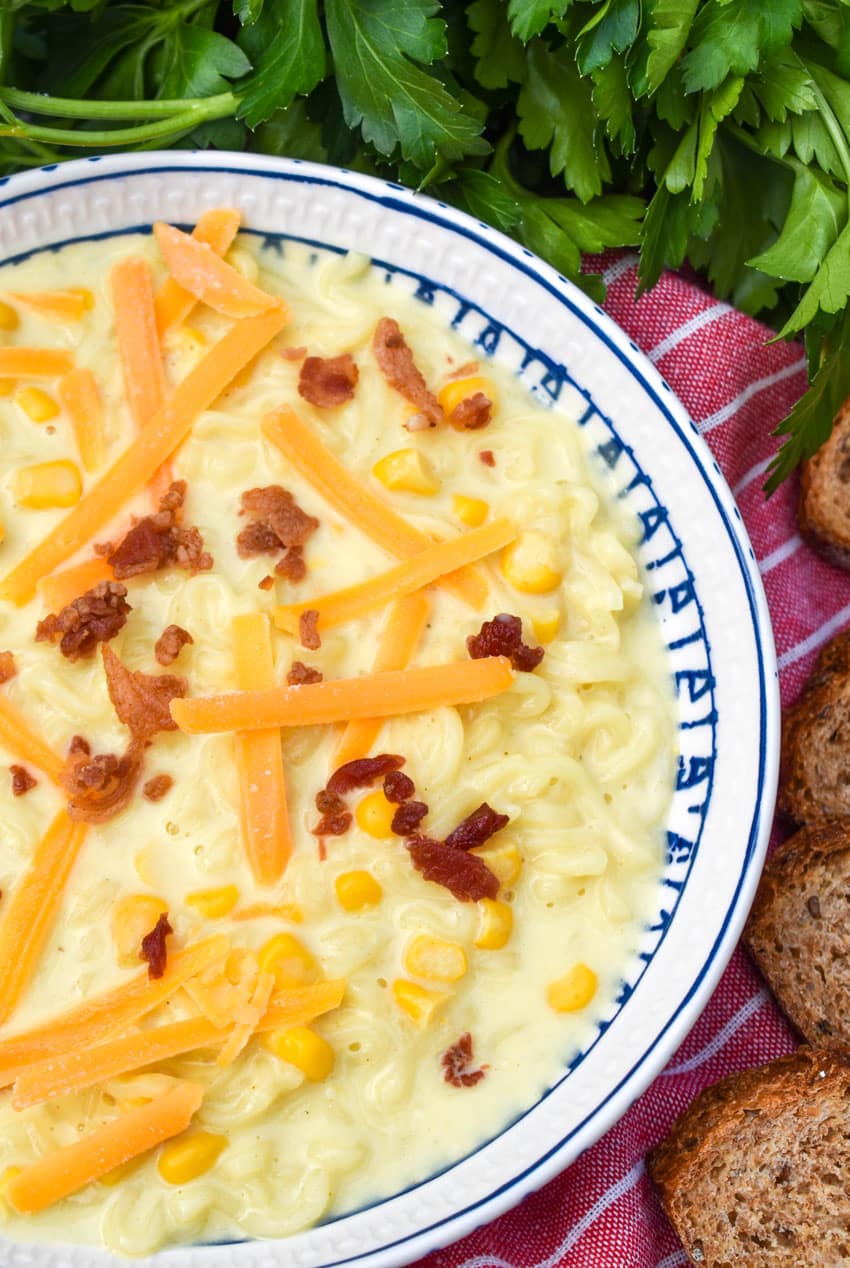 ramen noodle chowder topped with shredded cheese and bits of bacon in a white and blue flecked bowl