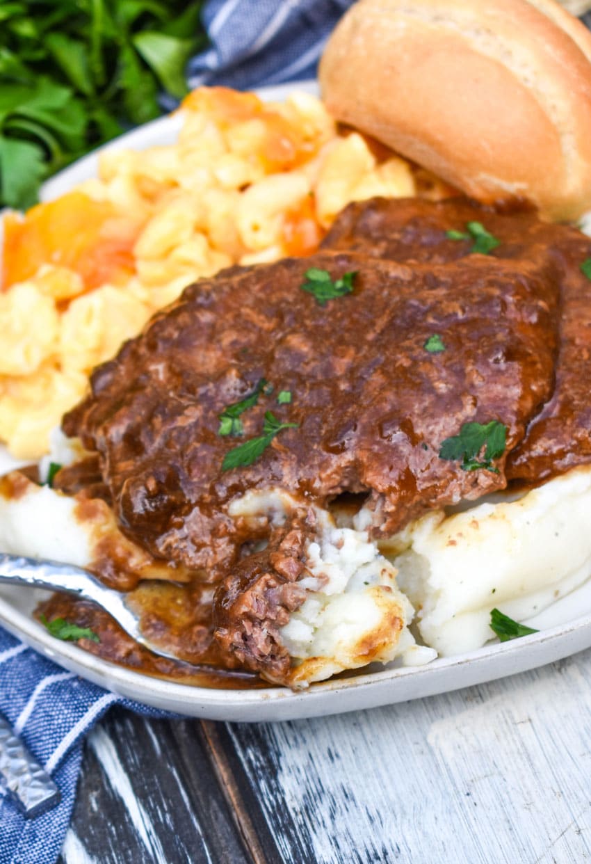 a silver fork scooping cube steak with brown gravy and mashed potatoes off a white plate