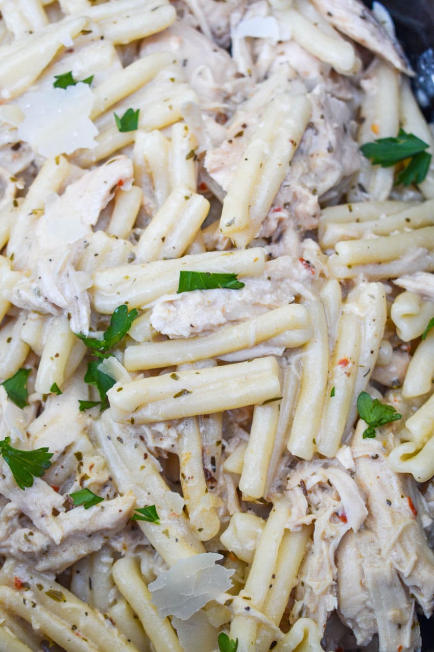a close up of garlic parmesan chicken and pasta in the black bowl of a slow cooker