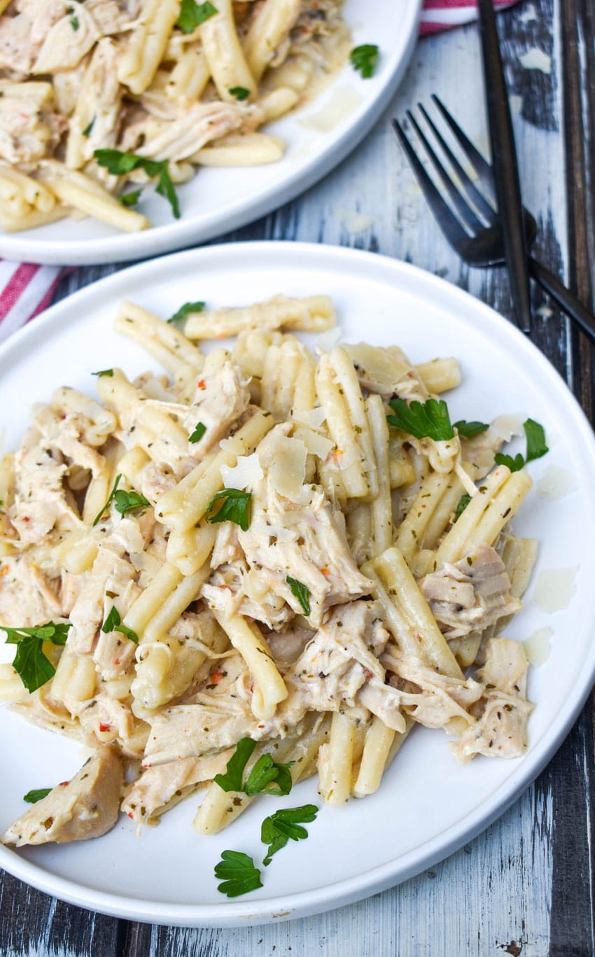 garlic parmesan chicken and pasta topped with fresh parsley leaves on a white plate