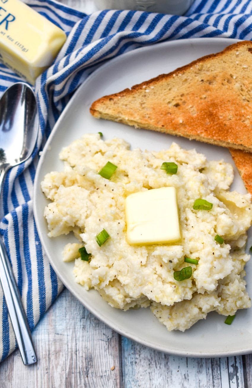 creamy slow cooker grits topped with a pat of butter and sliced green onions on a white plate with slices of toast on the side