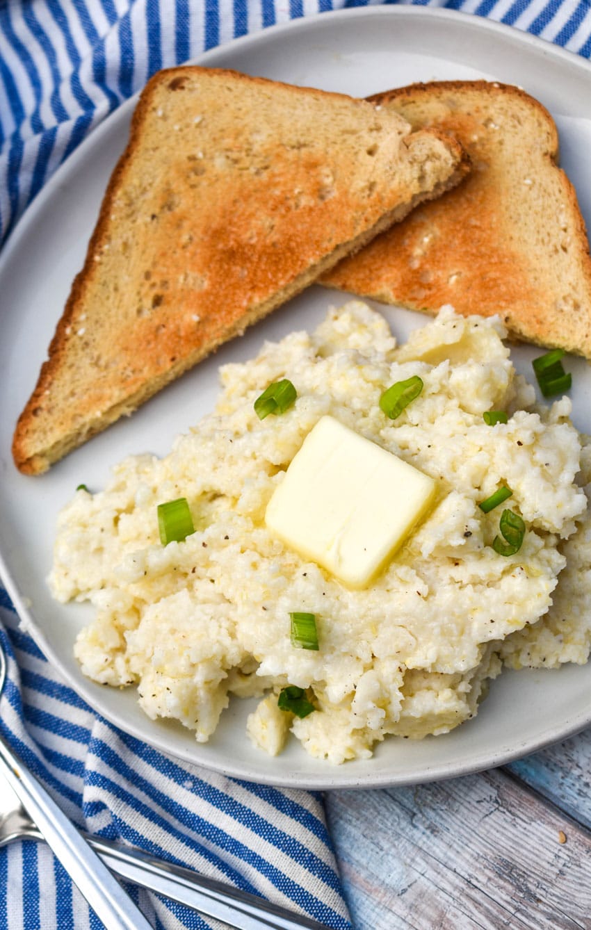 creamy slow cooker grits topped with a pat of butter and sliced green onions on a white plate with slices of toast on the side