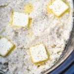 creamy slow cooker grits topped with melting pats of butter in a black crock