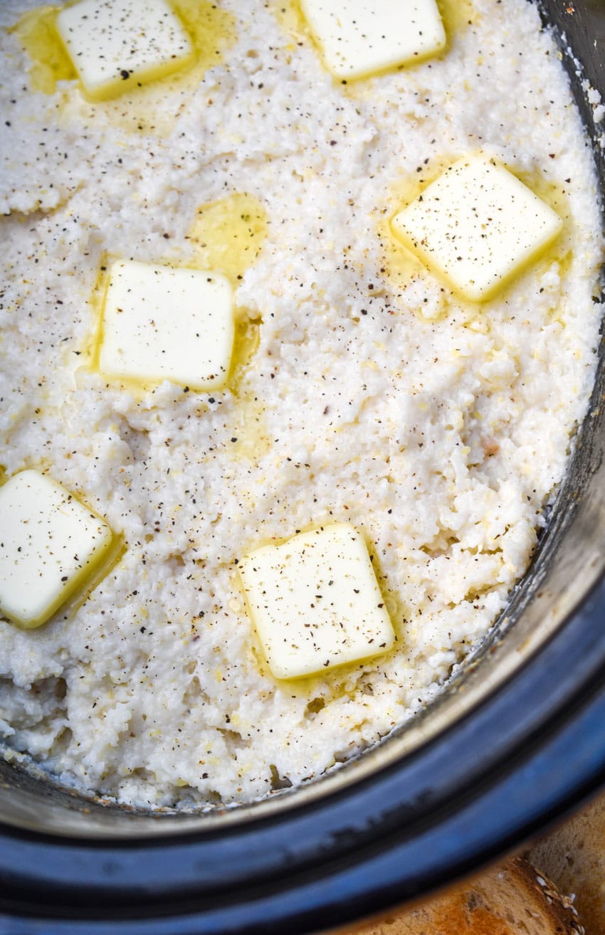 Creamy Crockpot Grits Recipe creamy slow cooker grits topped with melting pats of butter in a black crock