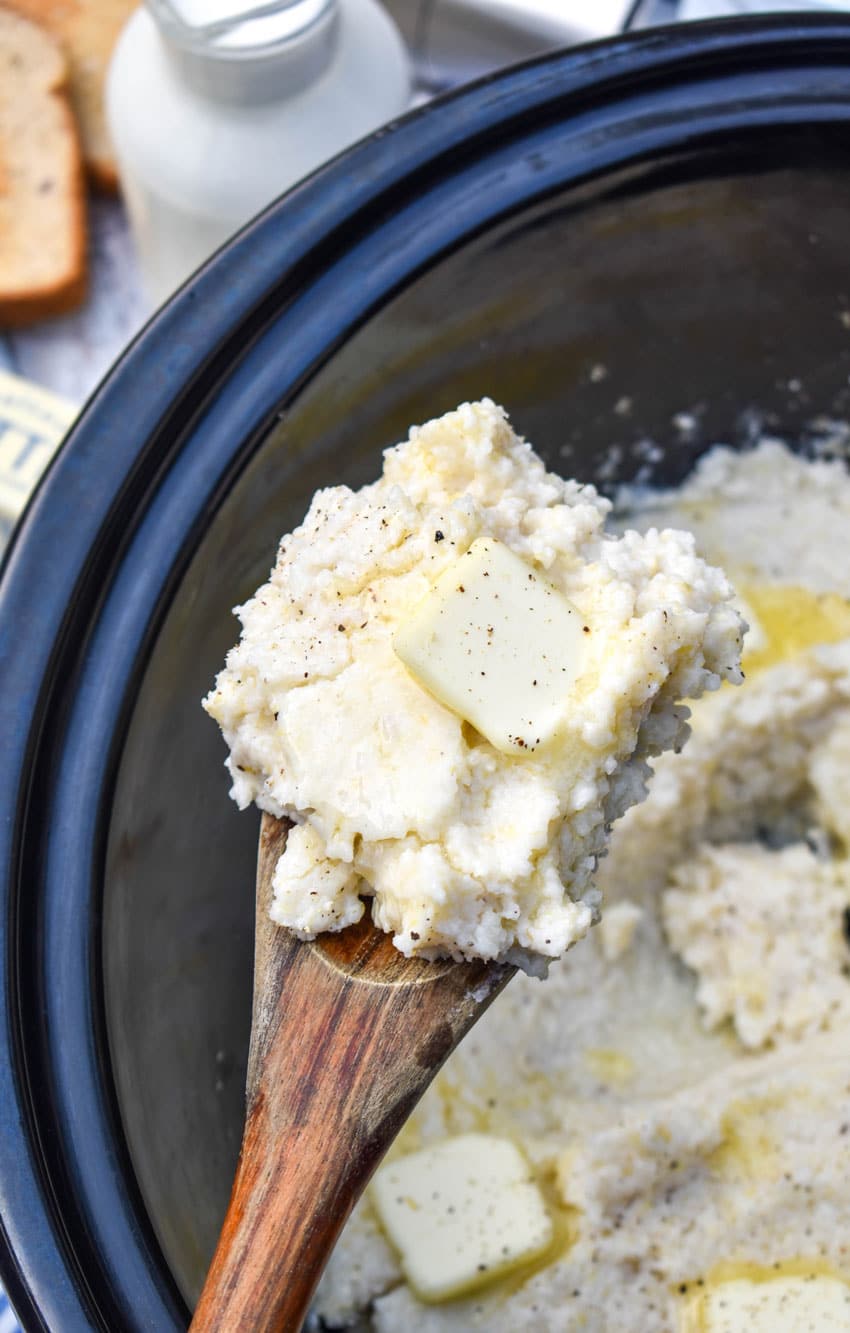 a wooden spoon holding up a scoop of creamy grits topped with butter
