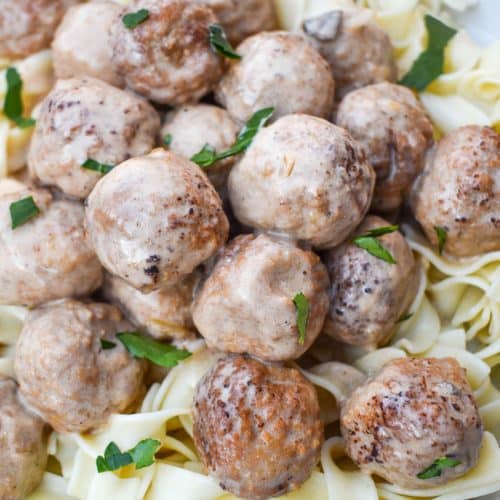 slow cooker swedish meatballs sprinkled with fresh parsley over cooked egg noodles on a white plate