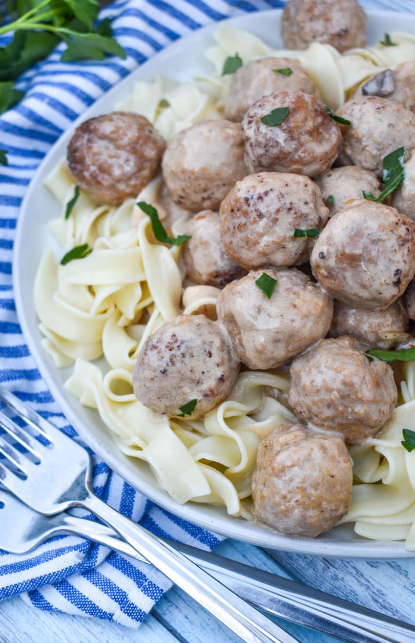 slow cooker swedish meatballs sprinkled with fresh parsley over cooked egg noodles on a white plate