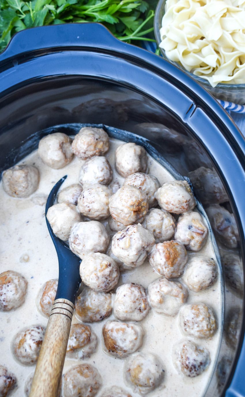 a black spoon scooping swedish meatballs out of a black crock