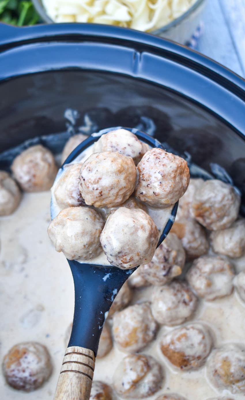 a black wooden handled spoon holding up a scoop of crockpot swedish meatballs