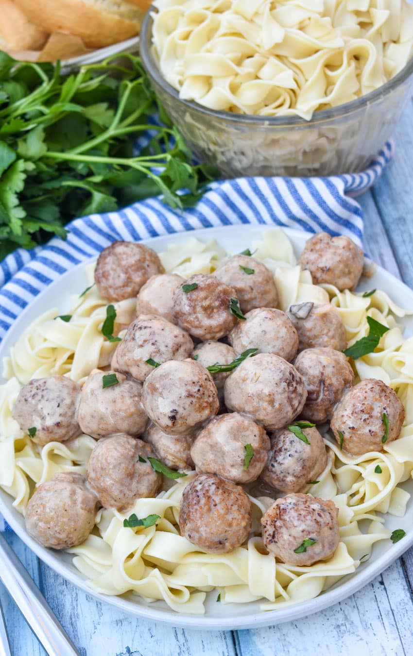 slow cooker swedish meatballs sprinkled with fresh parsley over cooked egg noodles on a white plate