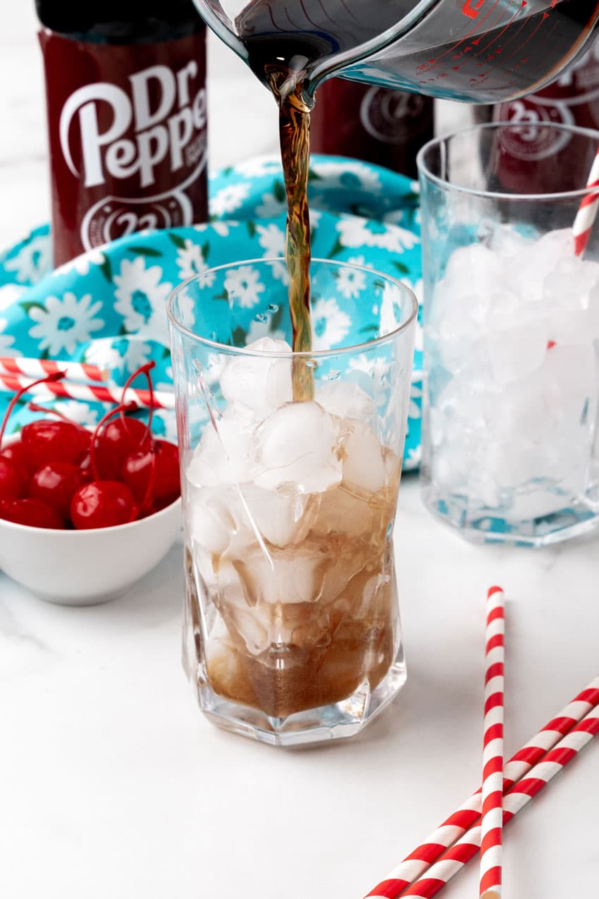 dr pepper soda being poured into a glass over ice