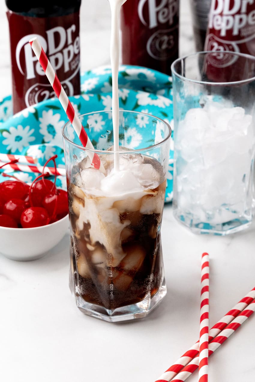 coffee creamer being poured into a glass of dr pepper