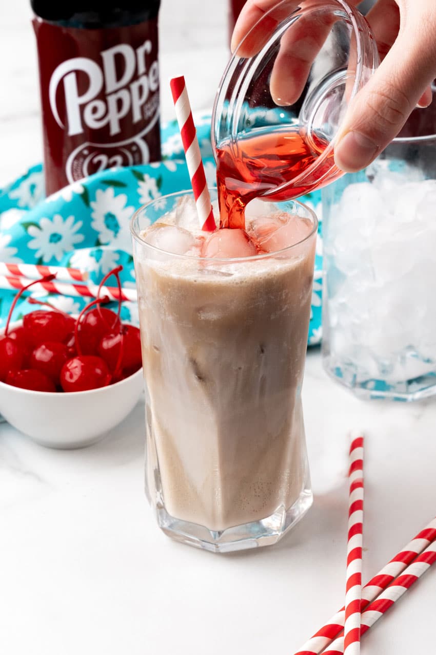 maraschino cherry juice being poured into a dirty soda in a glass