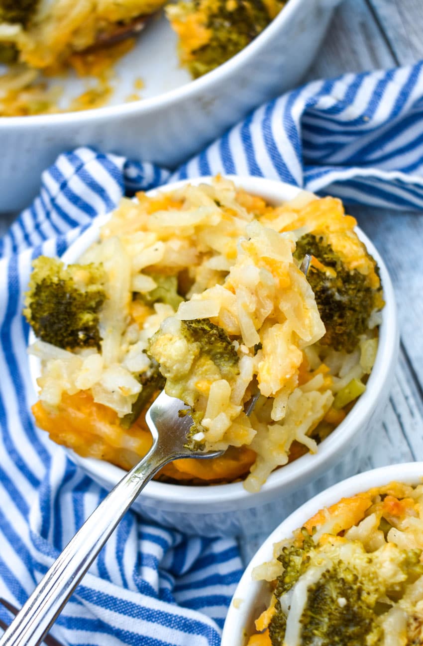 a silver fork scooping cheesy broccoli potato casserole out of a small white bowl