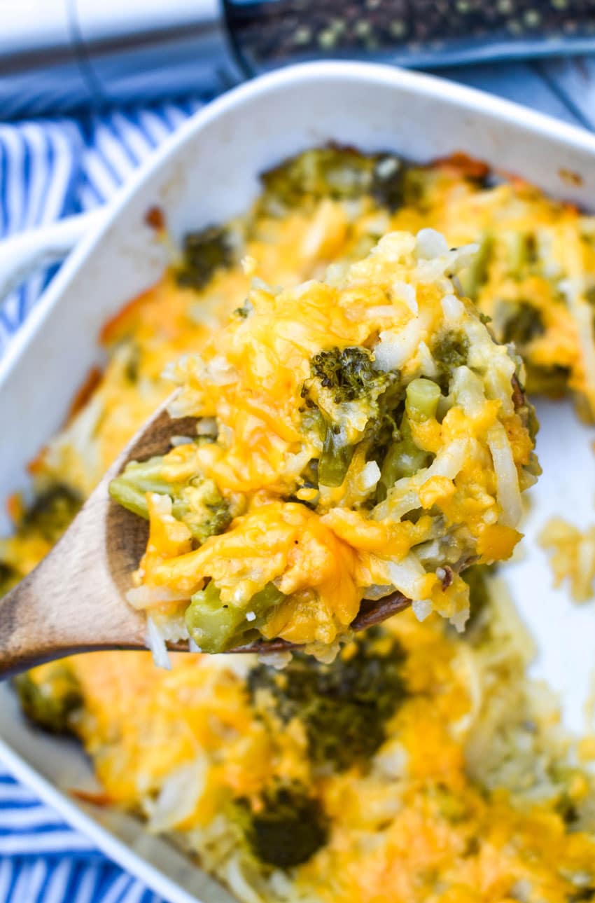 a wooden spoon holding up a scoop of cheesy broccoli potato casserole