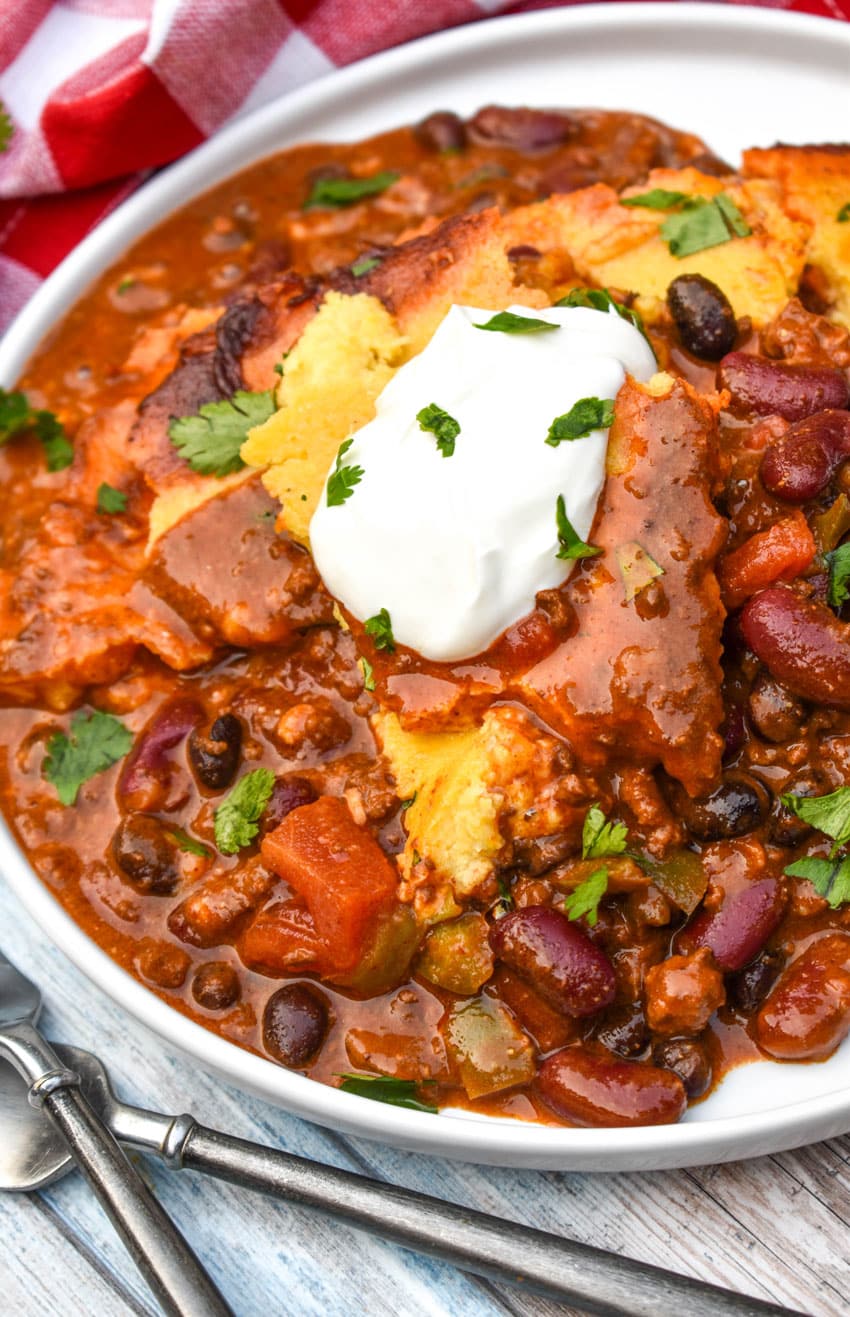 chili cornbread casserole topped with sour cream and fresh herbs on a white plate