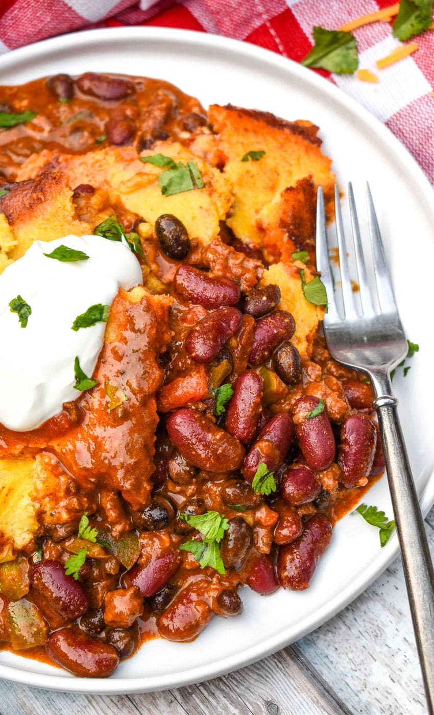 chili cornbread casserole topped with sour cream and fresh herbs on a white plate