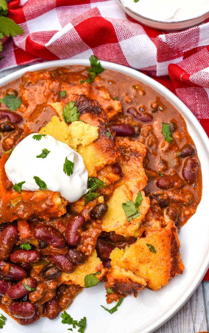 chili cornbread casserole topped with sour cream and fresh herbs on a white plate