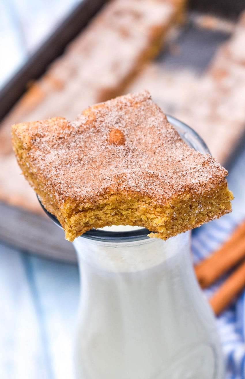 a bitten churro bar square resting on top of a glass bottle filled with milk