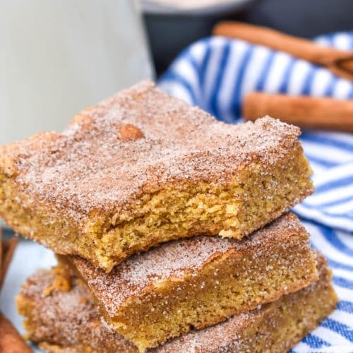 a stack of three churro bar squares on a wooden table with a glass bottle of milk in the background