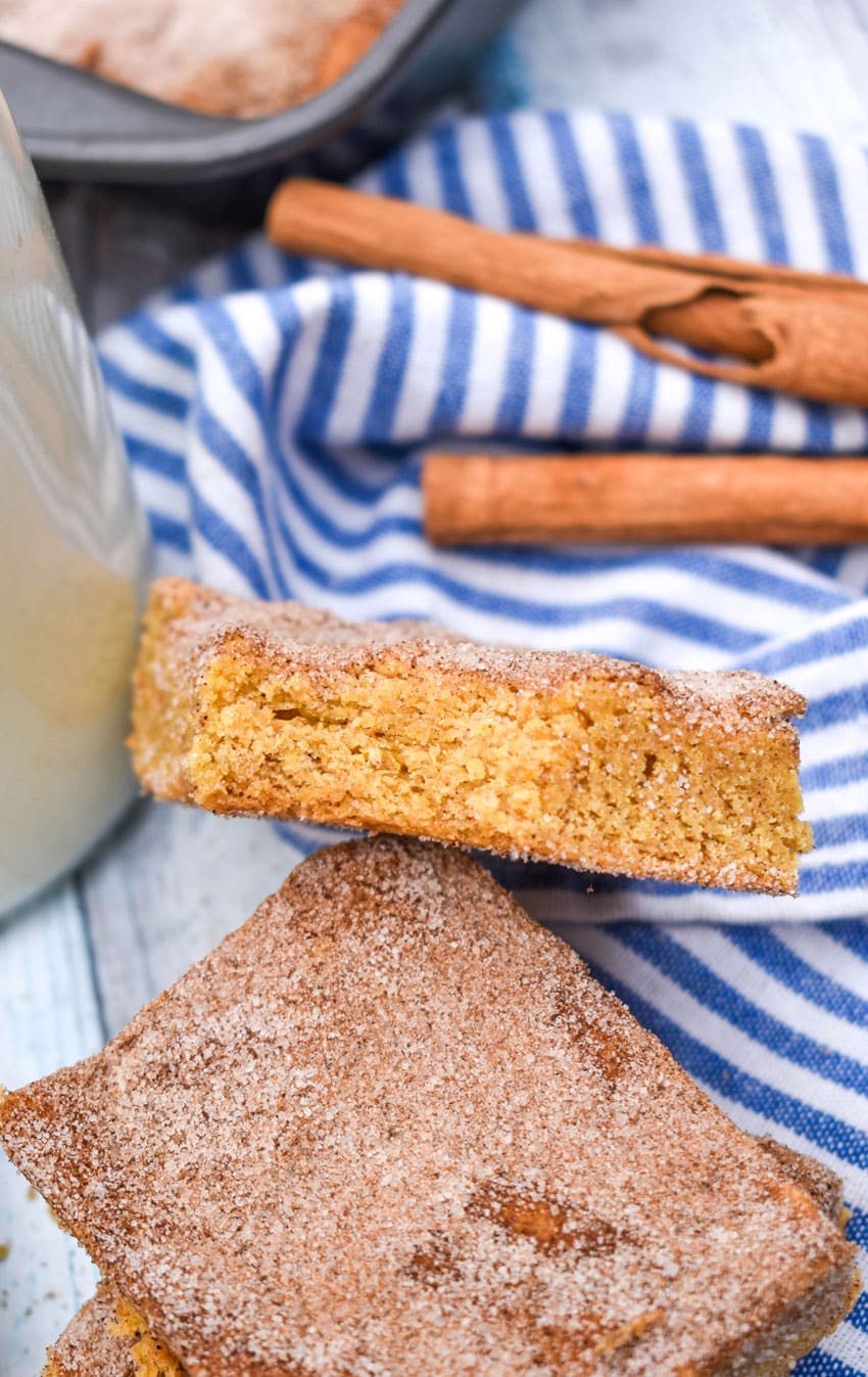 a stack of churro bar squares on a wooden table with a glass bottle of milk in the background