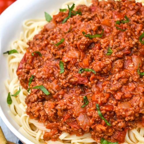 THREE MEAT PASTA SAUCE OVER COOKED SPAGHETTI PASTA IN A WHITE SERVING BOWL