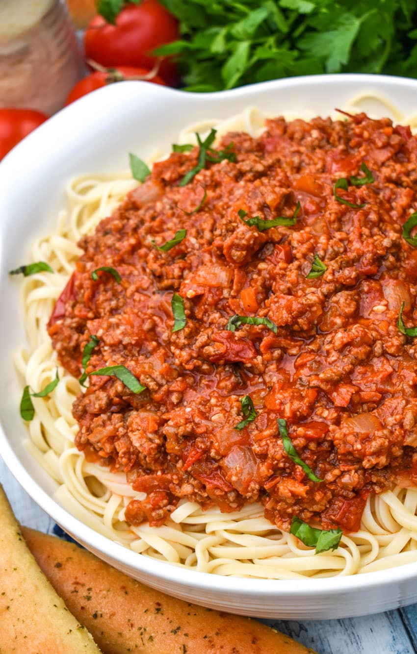 THREE MEAT PASTA SAUCE OVER COOKED SPAGHETTI PASTA IN A WHITE SERVING BOWL
