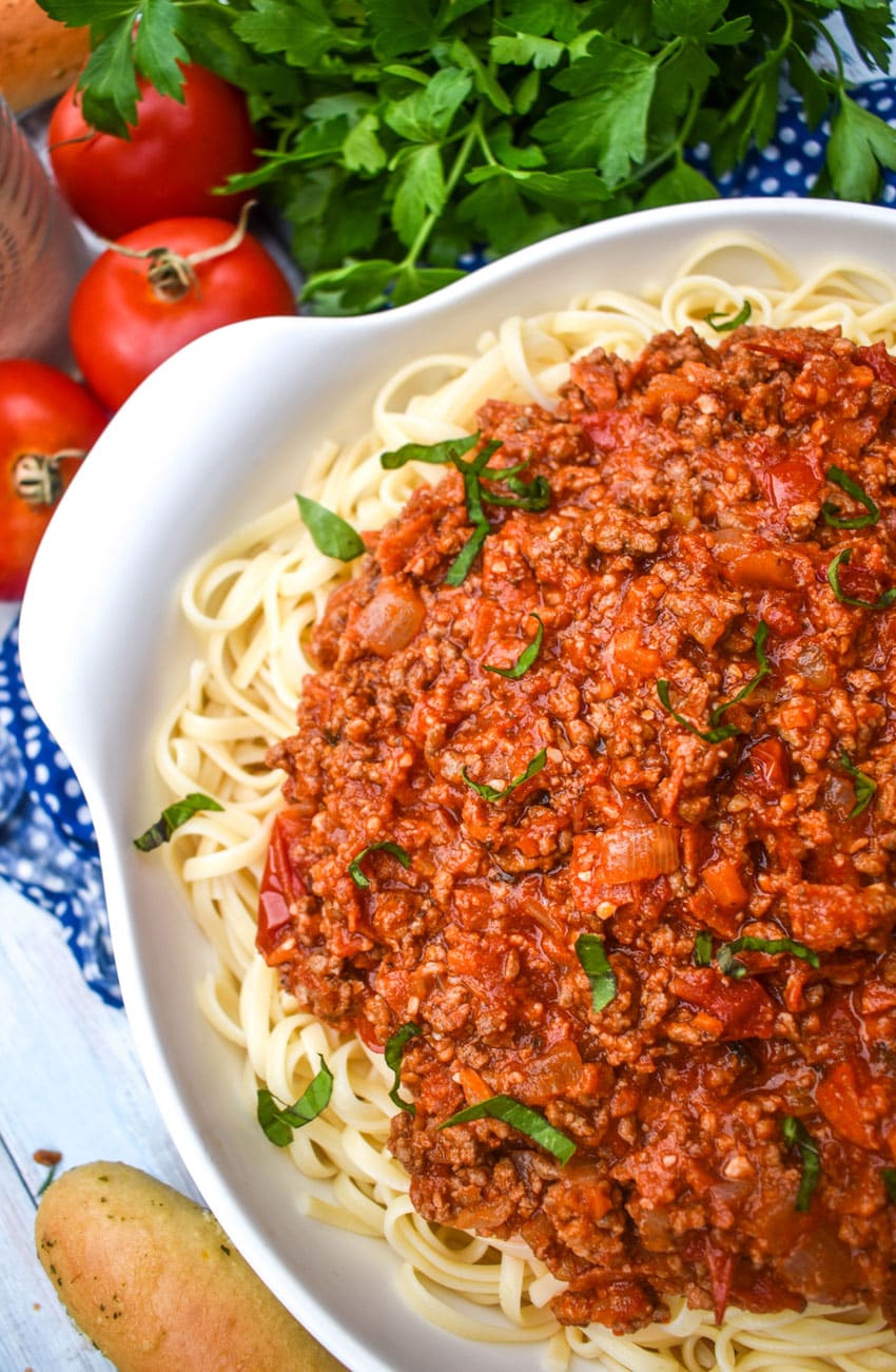 OLIVE GARDEN'S MEAT SAUCE RECIPE OVER COOKED SPAGHETTI PASTA IN A WHITE SERVING BOWL