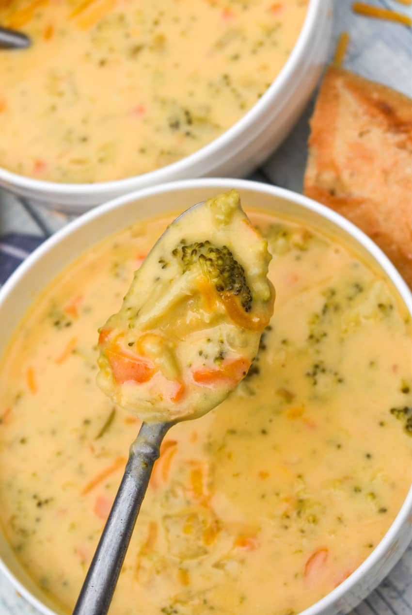 a silver spoon holding a scoop of creamy broccoli cheddar soup above a white bowl