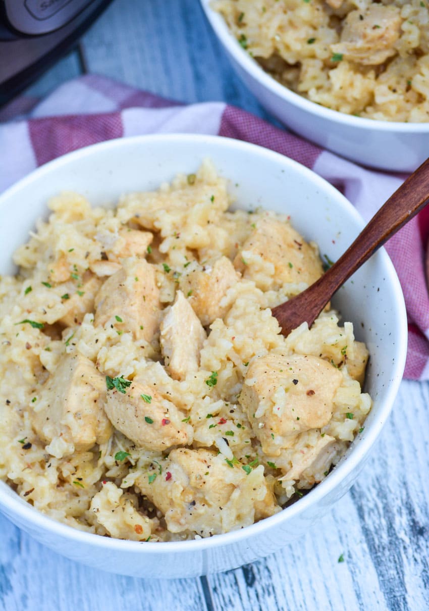 one pot creamy chicken and rice in a white bowl with a wooden spoon on the side