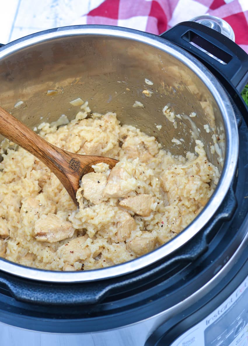 a wooden spoon scooping creamy chicken and rice out of an instant pot pressure cooker