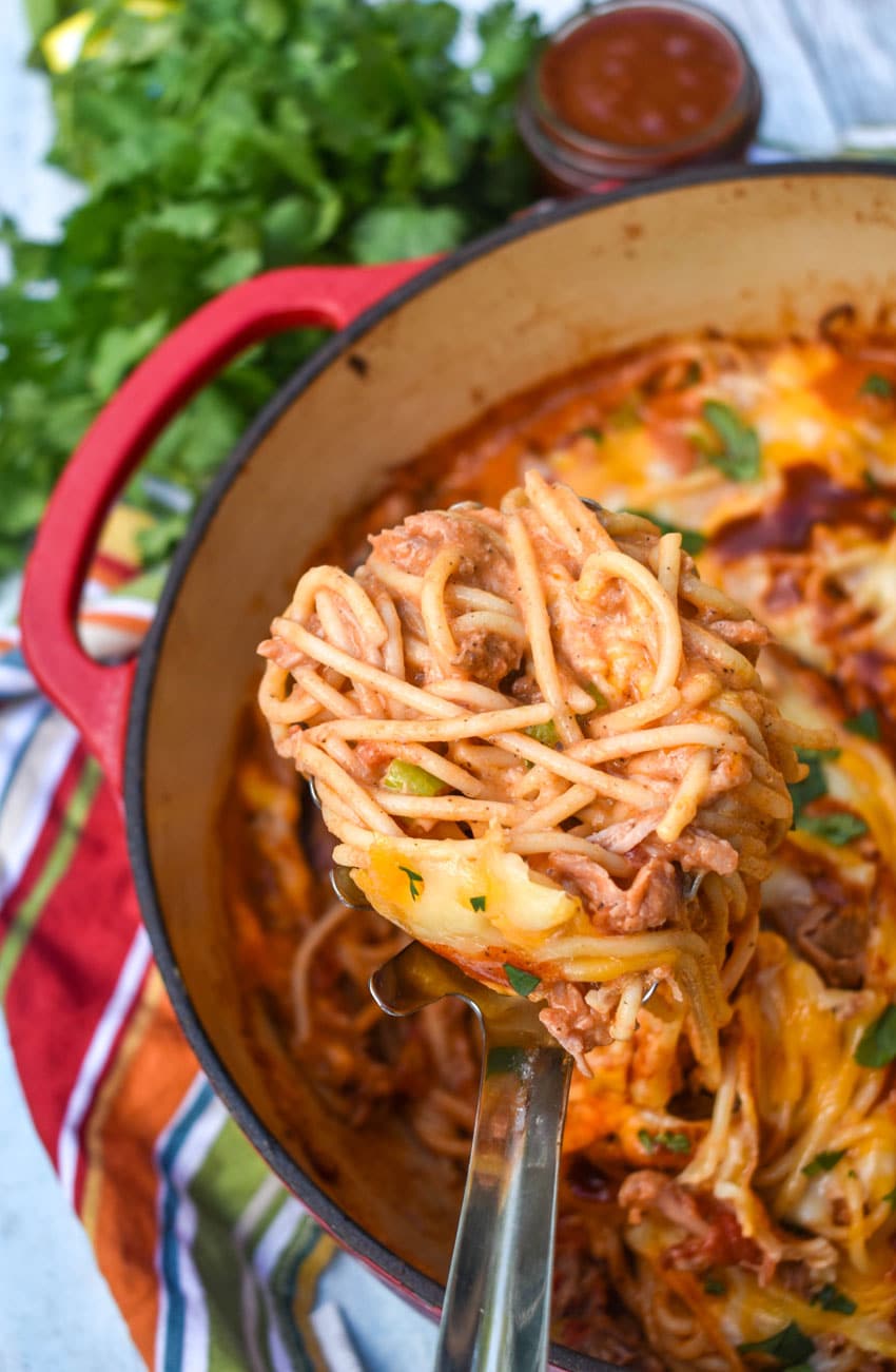 a silver spatula scooping barbecue pulled pork pasta out of a large red dutch oven