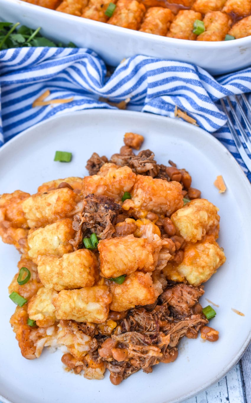 a scoop of pulled pork tater tot casserole topped with sliced green onions on a white plate