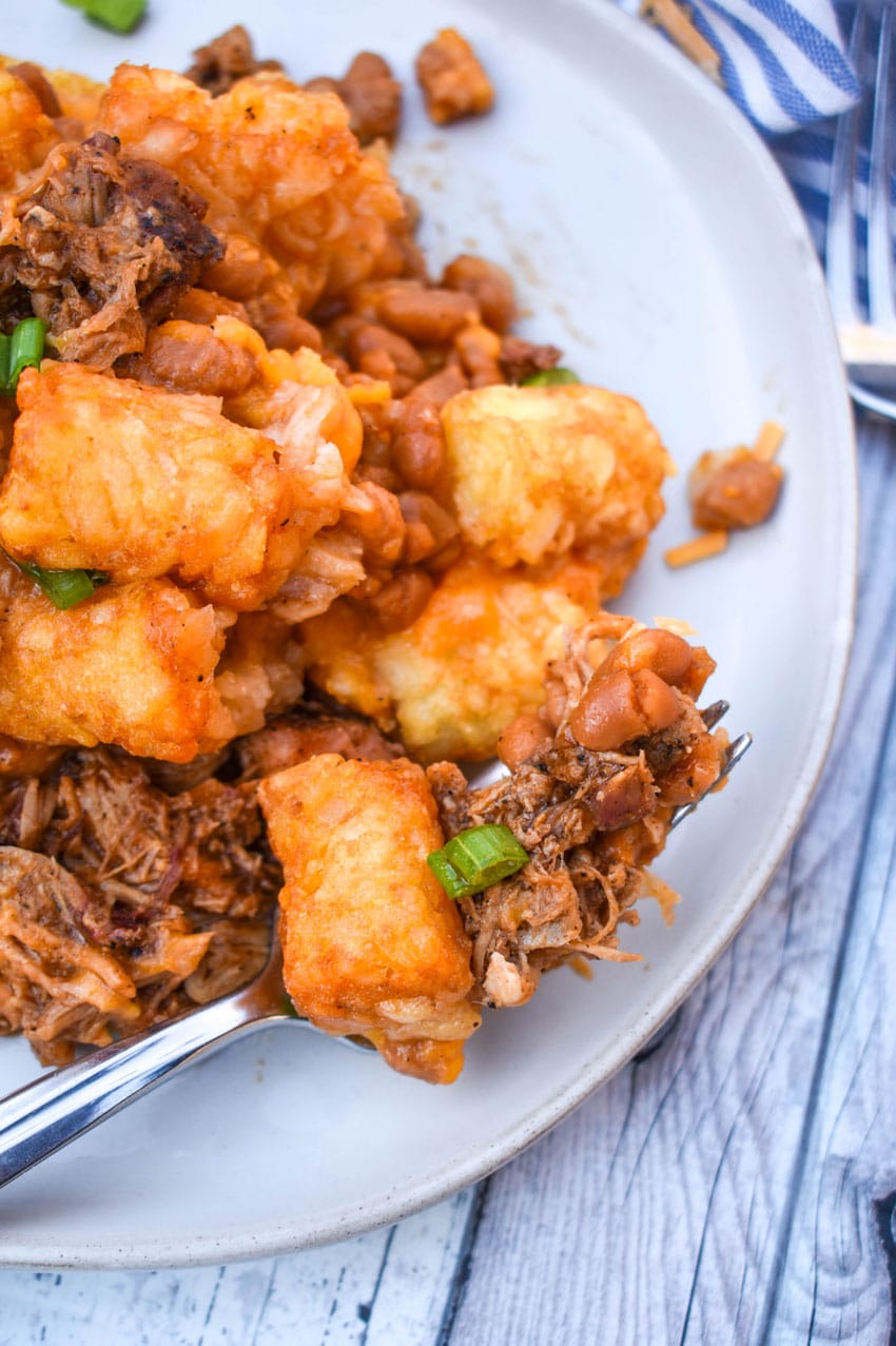a silver fork holding a scoop of barbecue tater tot casserole resting on the edge of a white plate