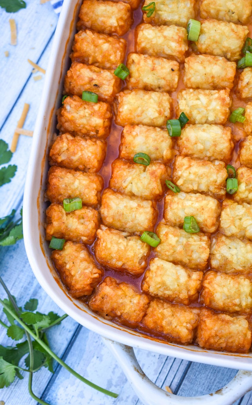 pulled pork tater tot casserole topped with sliced green onions in a white baking dish