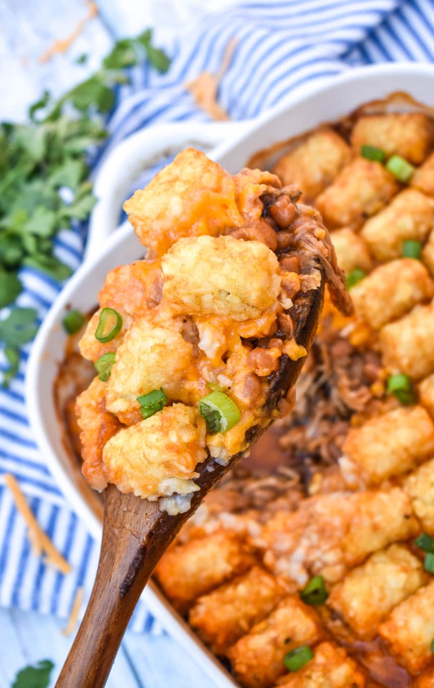 Pulled Pork Tater Tot Casserole a wooden spoon holding up a scoop of pulled pork tater tot casserole
