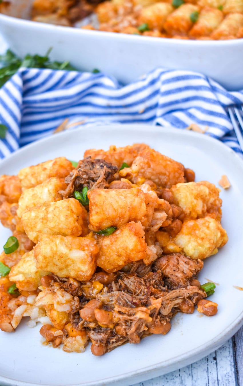 a scoop of pulled pork tater tot casserole topped with sliced green onions on a white plate