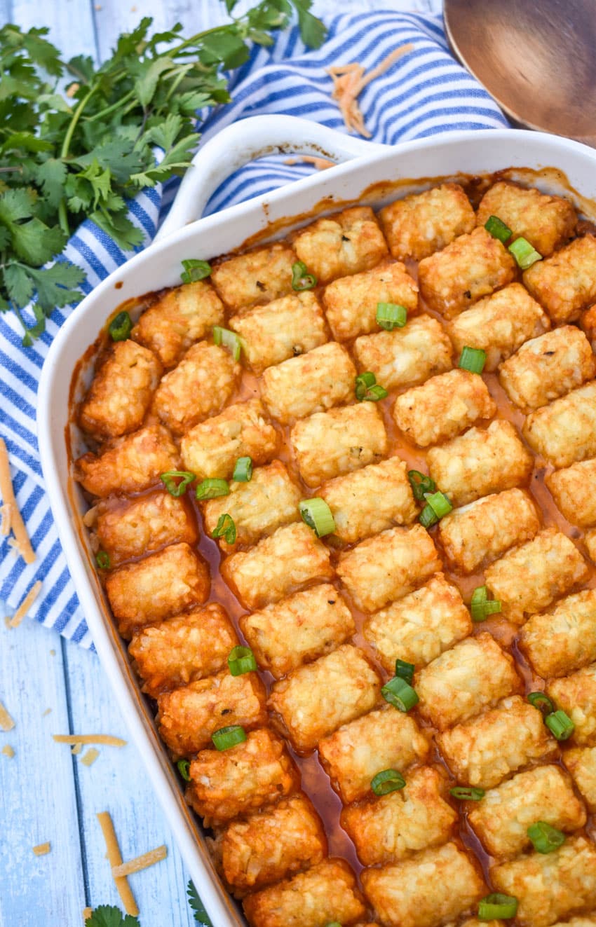 pulled pork tater tot casserole topped with sliced green onions in a white baking dish