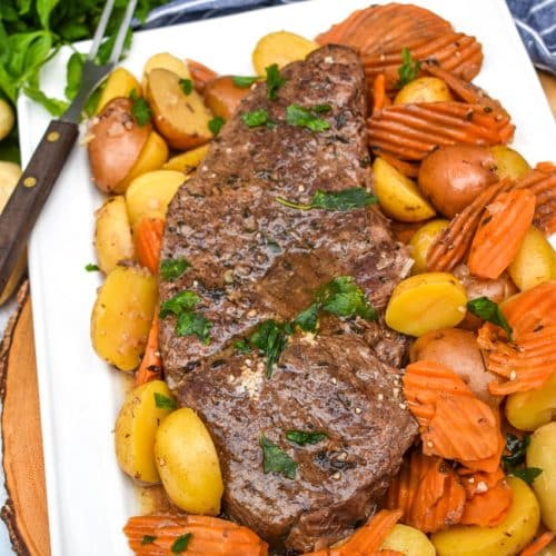 THE BEST SLOW COOKER POT ROAST RECIPE SURROUNDED BY COOKED CARROTS AND POTATOES ON A WHITE PLATTER
