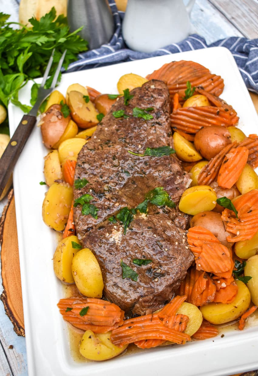 THE BEST SLOW COOKER POT ROAST RECIPE SURROUNDED BY COOKED CARROTS AND POTATOES ON A WHITE PLATTER