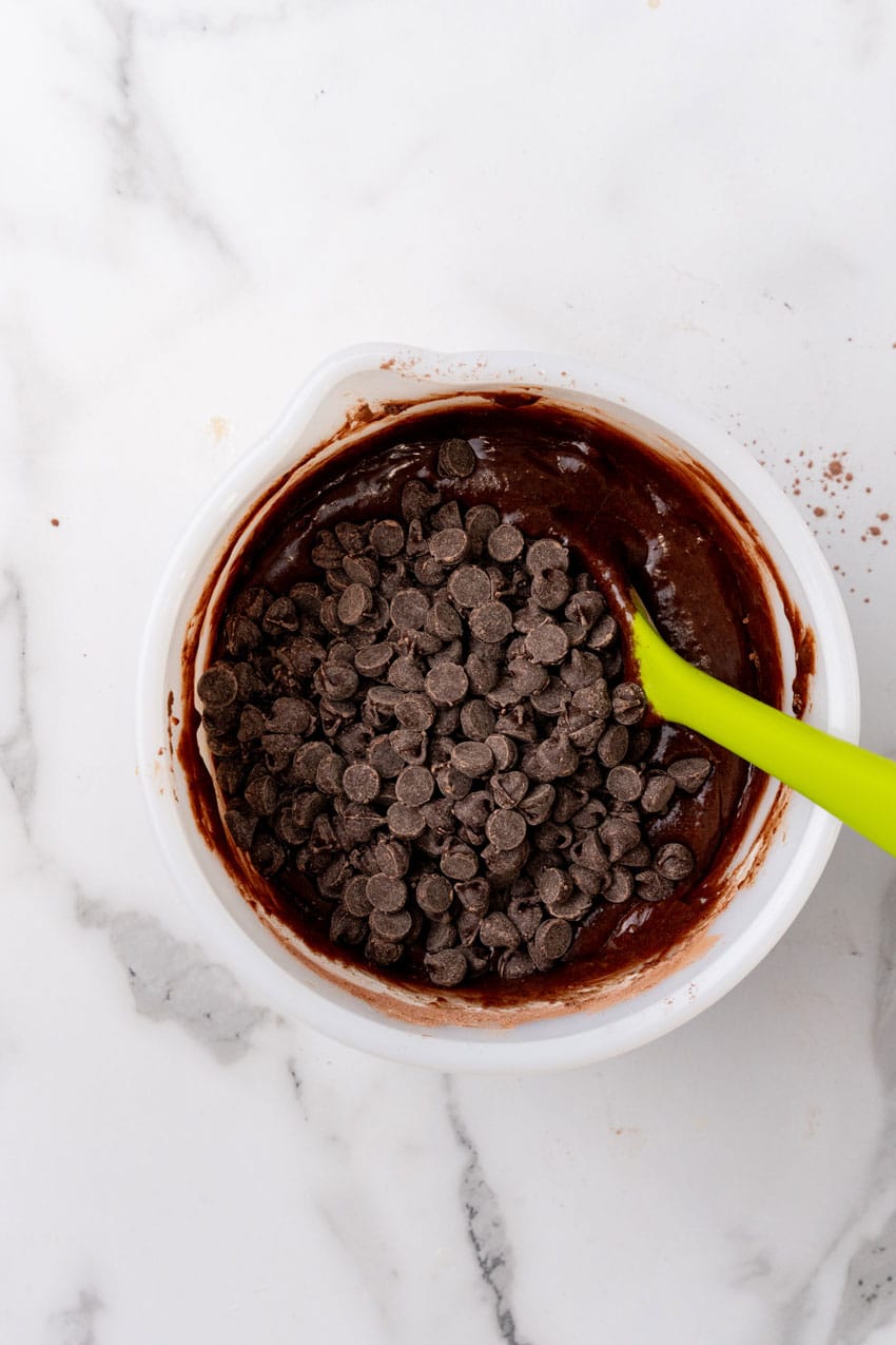 chocolate chips on top of brownie batter in a white mixing bowl