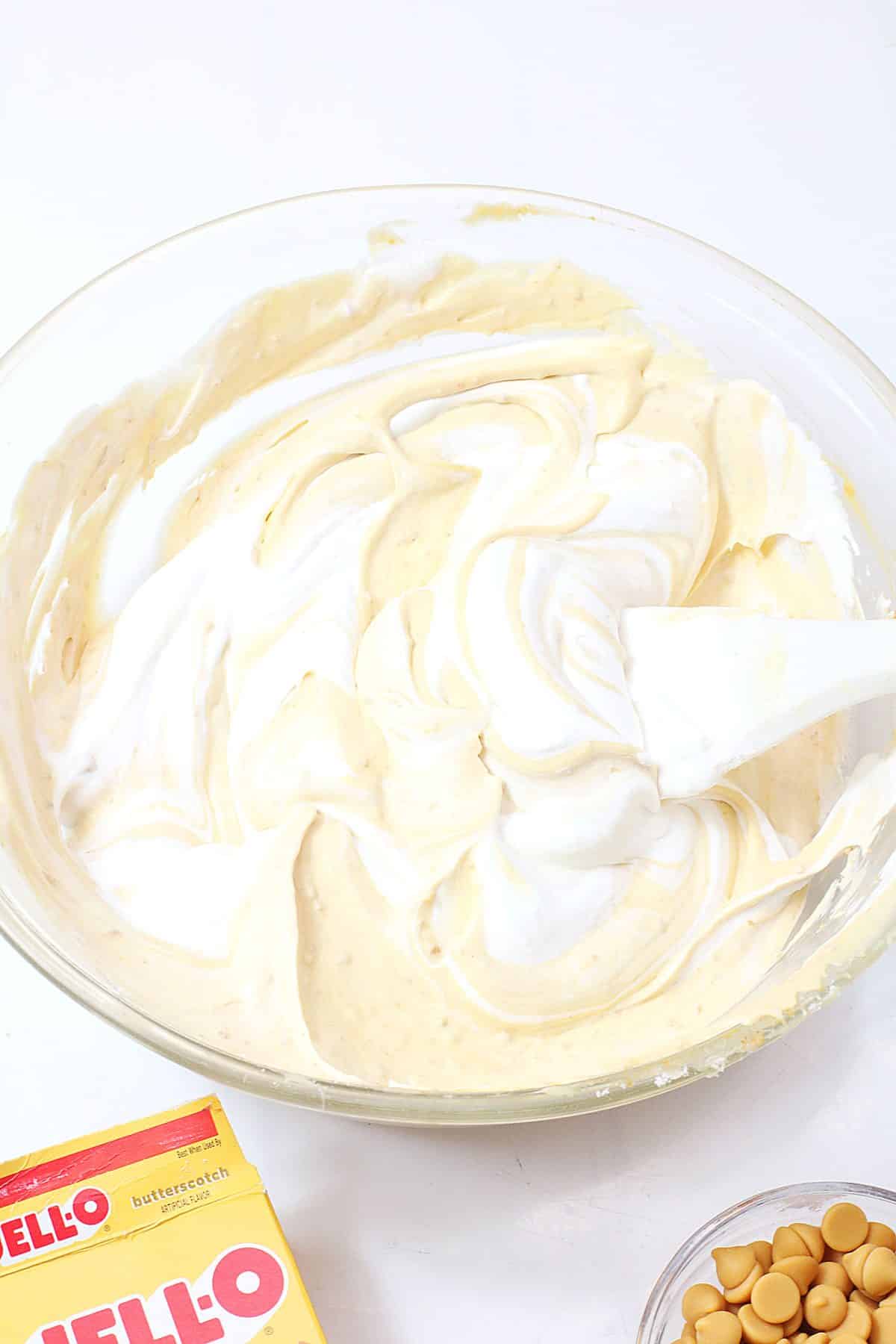 cool whip and butterscotch pudding being mixed together in a glass mixing bowl